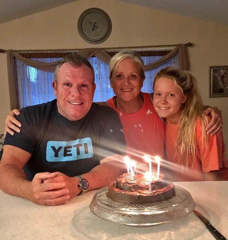 Three people smiling around a lit birthday cake