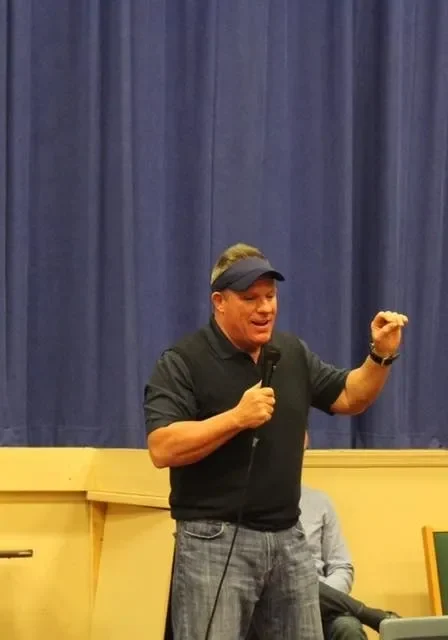 Man speaking on stage with blue curtain.