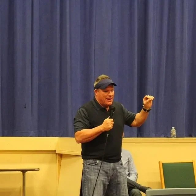 Man wearing cap speaking on stage with microphone