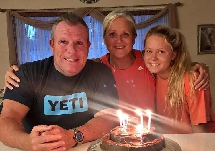 Three people smiling around a lit birthday cake